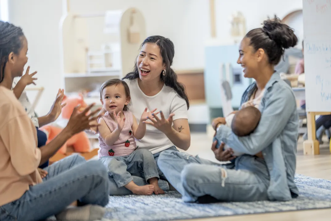 three women and their young children sit in a circle, some clapping and smiling
