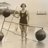 A black and white gelatin silver print of Gertrude Ederle standing on the shore with a 1920s flotation device.