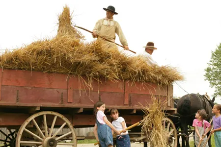 Young guests and living history staffers unload hay.
