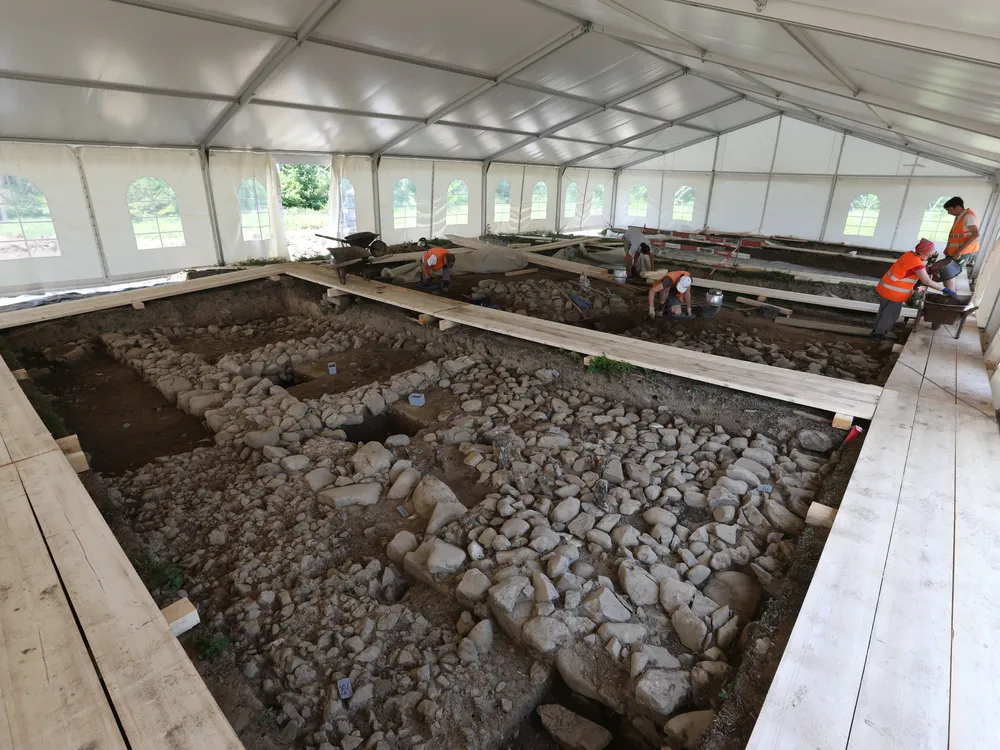 Large white tent covering archaeological dig of stones