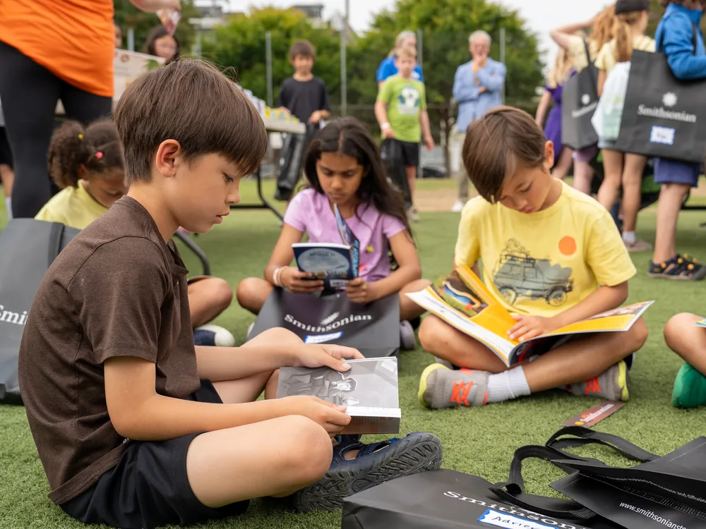 A group of children sit on the grass to read silently to themselves