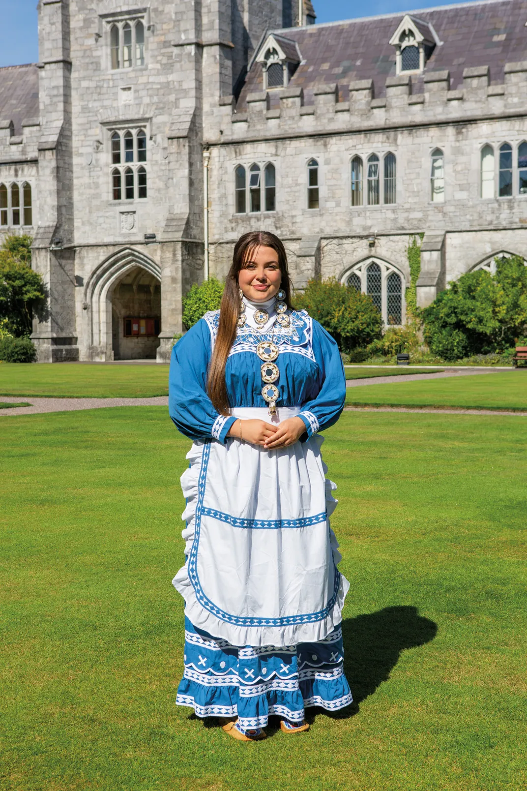 a woman in a dress stands for a portrait in a quadrale with a brick building behind her