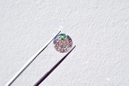 Silver tweezers hold a small diamond against a white background.