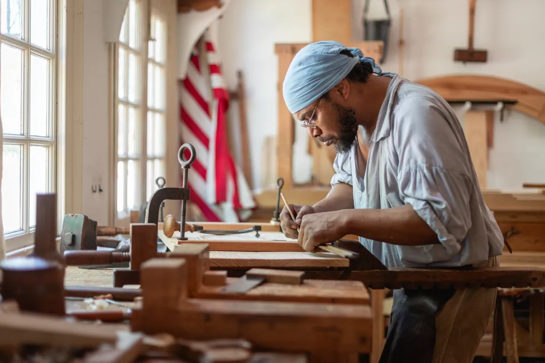 A man bending over a work bench with windows and an American flag in the background