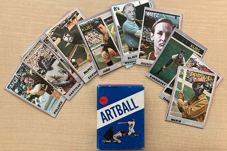 Baseball cards with faces of artists superimposed on them fanned out on a desk above a blue box with text that reads ARTBALL, an image of a batter, catcher, and umpire, with a red circle that says set 1.