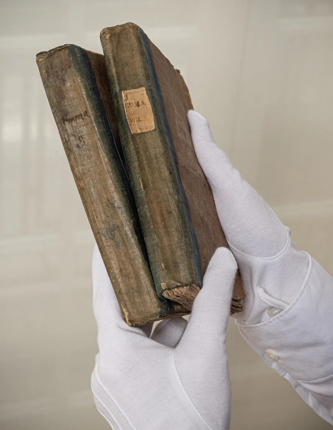 White gloved hands holding up two older books