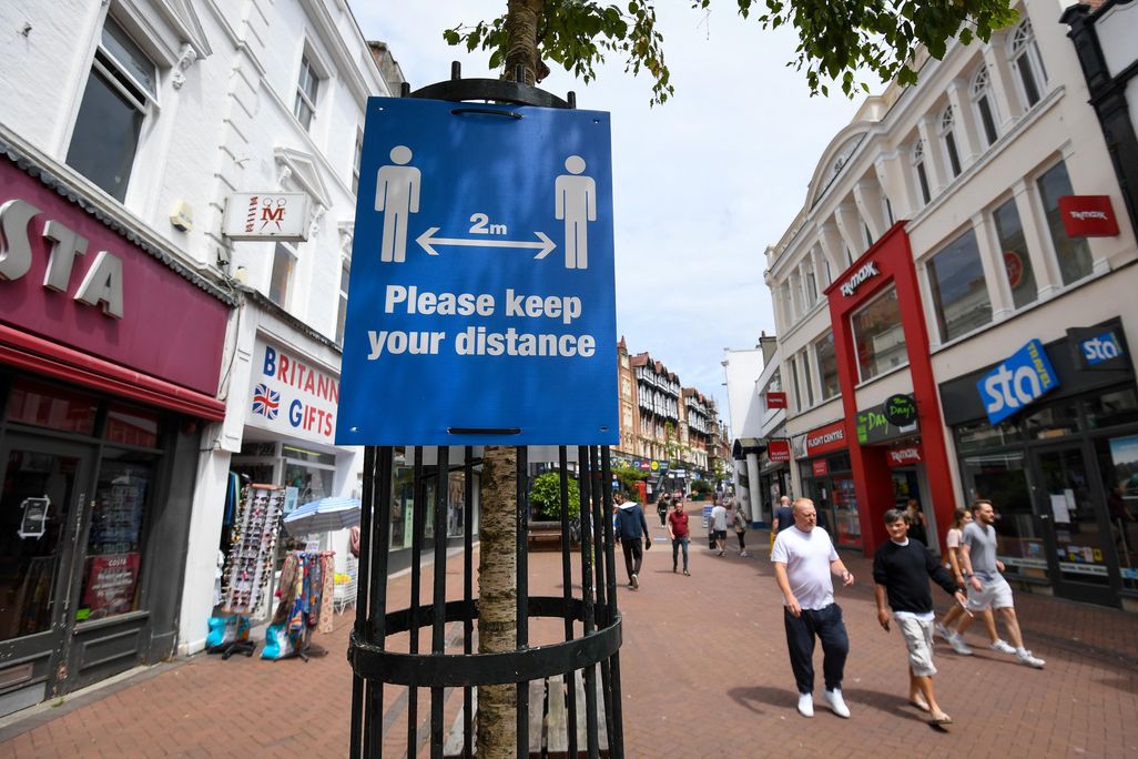 A sign reads "Please keep your distance" on a street with small shops in Bournemouth, U.K.