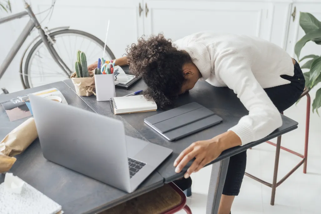 A woman puts her head down on a desk amid her laptop and notebooks