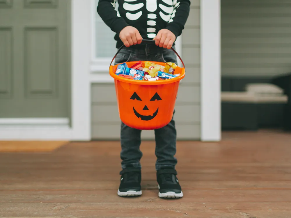 A child wearing a skeleton costume for Halloween holds candy 