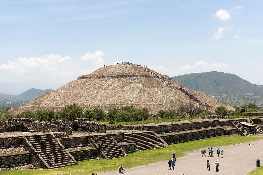 A view of the Pyramid of the Sun at Teotihuacan, a huge pyramid that stands several stories tall over an expansive avenue populated by tourists