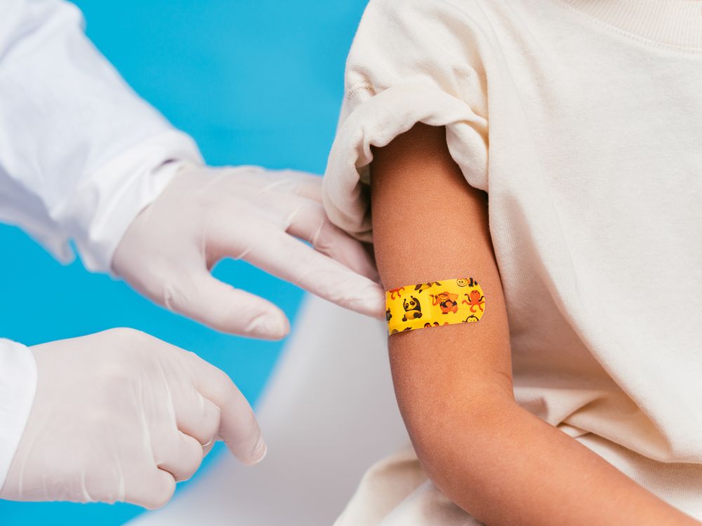 Gloved doctors hands and a child's right arm with an orange bandaid