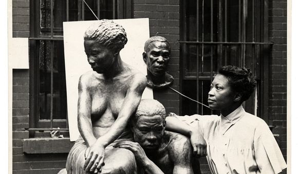 A black and white photograph of artist Augusta Savage standing next to her sculpture