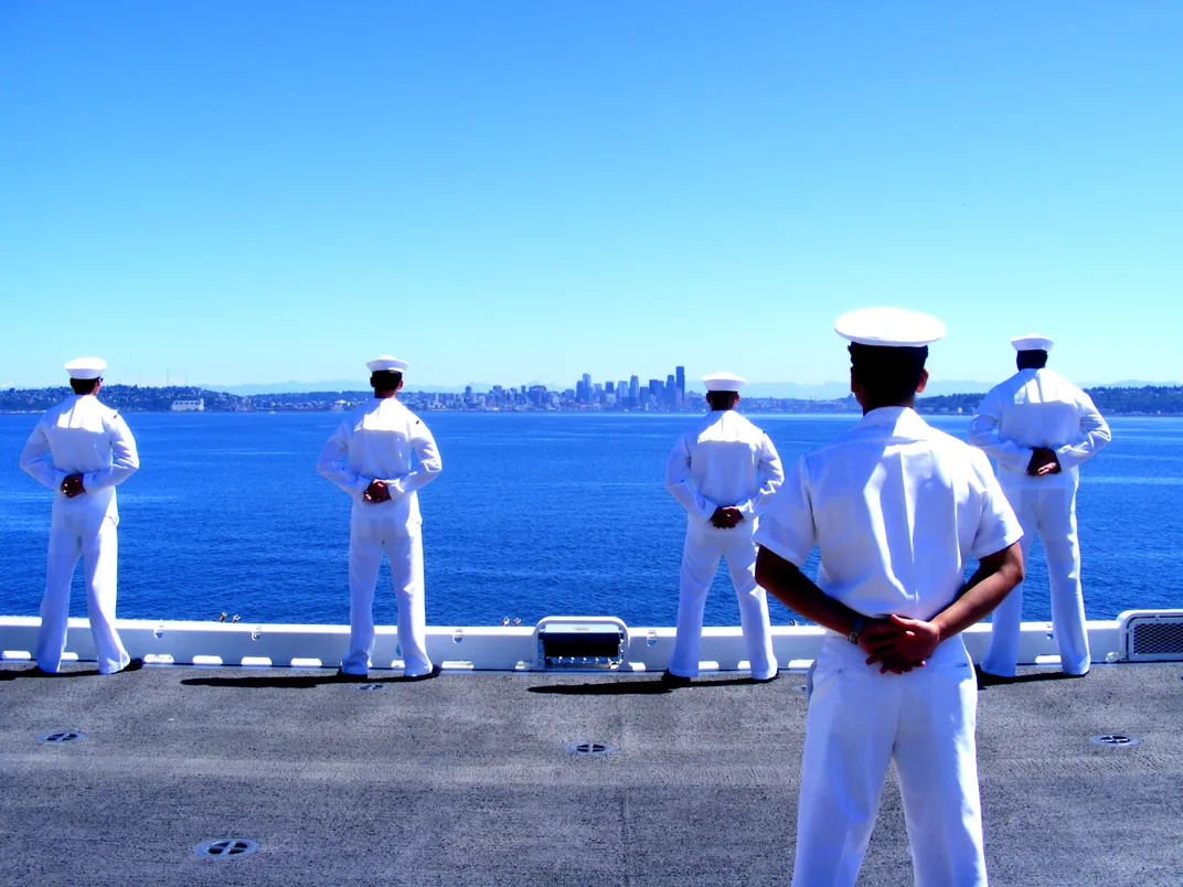 sailors wearing white standing next to the water