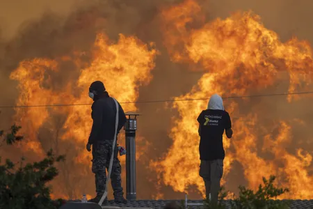 Flames reach the Greek village of Gennadi, where residents stand on roofs to try to save their homes with water hoses.