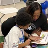 A woman reads with a young boy, the book says "wheelbarrow" in big letters