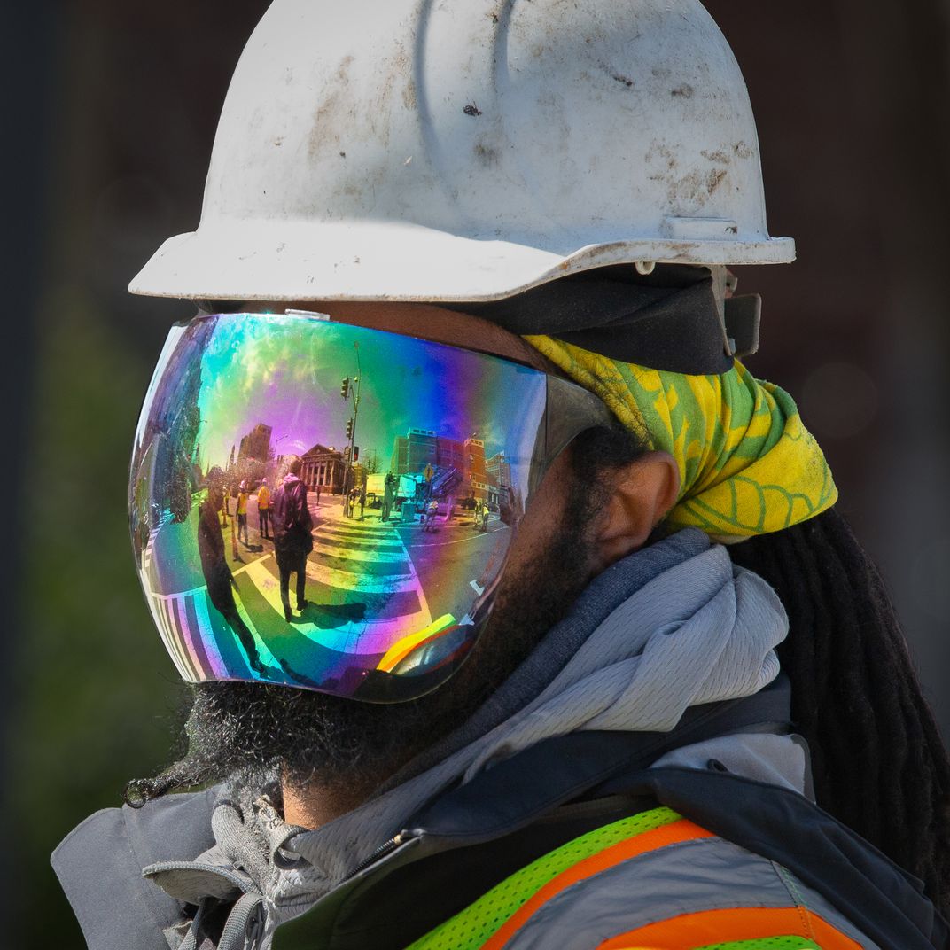 2 - This worker demonstrates multitasking at its best. While wearing a mask to protect himself from Covid-19 and the sun, he ushers people across the street in a construction zone.