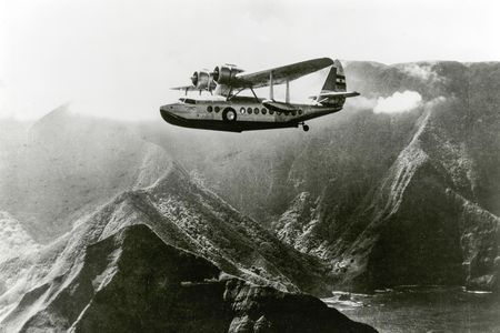 An Inter-Island Airways Sikorsky S-43 flies past Molokai mountains and lagoon.
