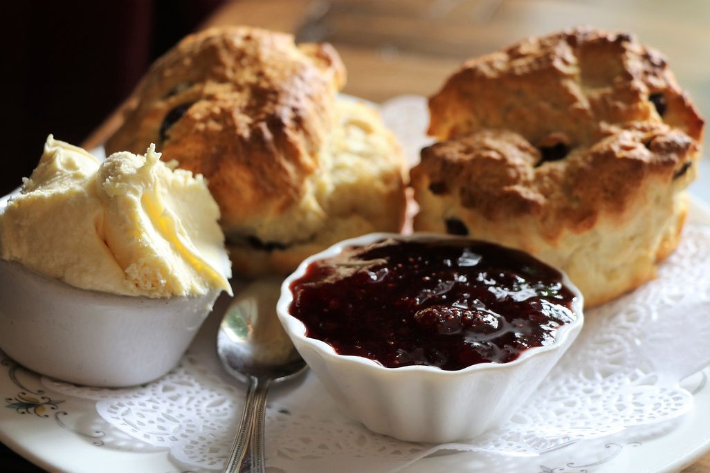 Two golden scones on a plate with clotted cream and strawberry jam
