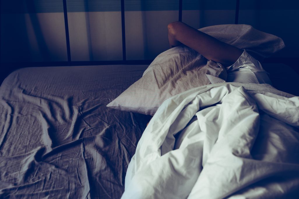 A person lying in bed holds a pillow over their head as they struggle to sleep