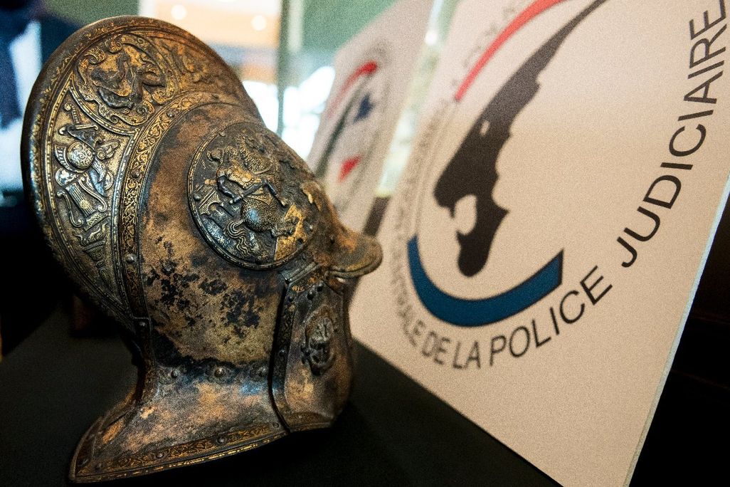 A close up look at an intricately carved helmet, with motifs of flowers, swords, torches and warriors on it