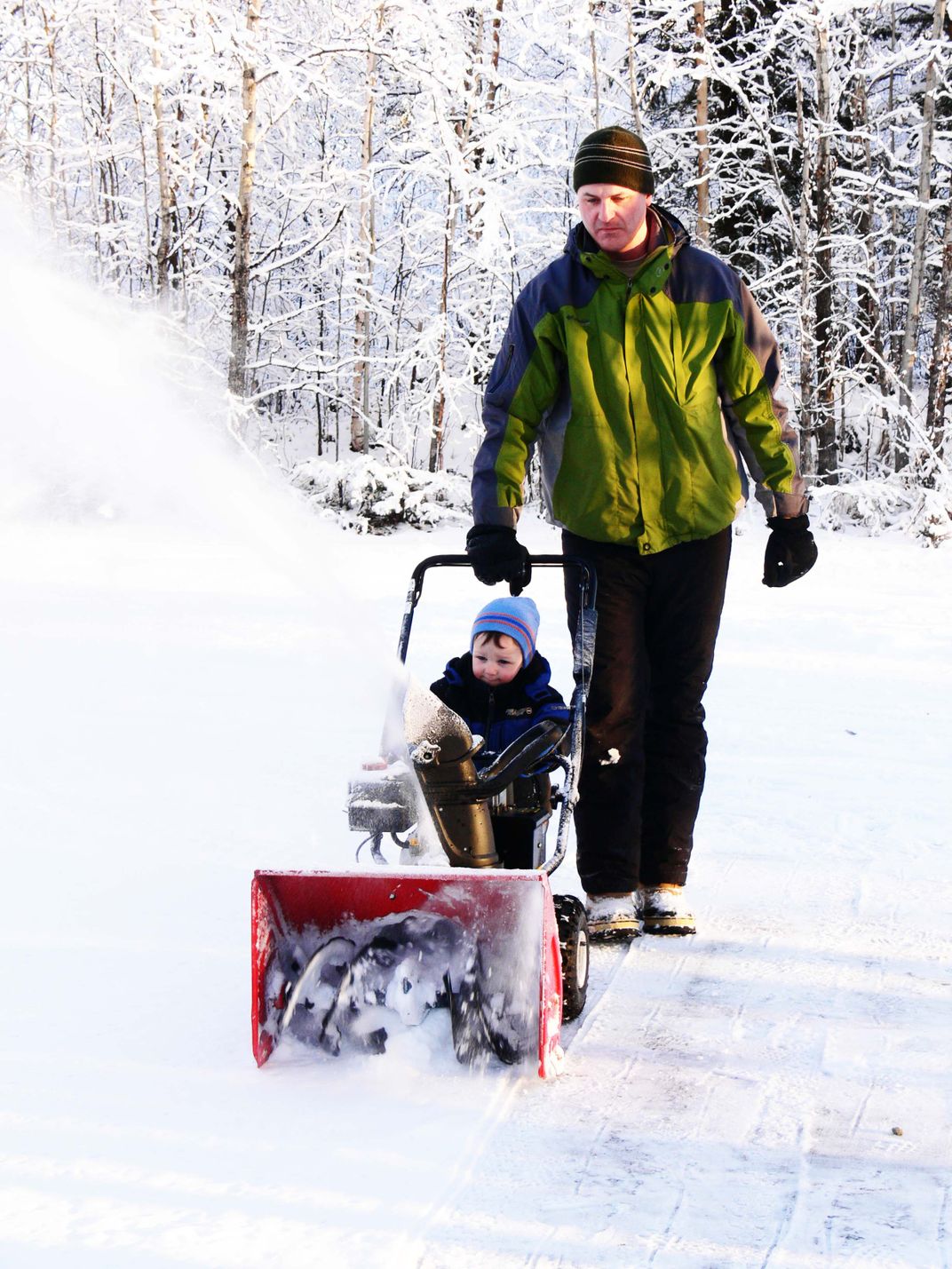 4 - A toddler seemingly shows his father how to properly use a snowblower.