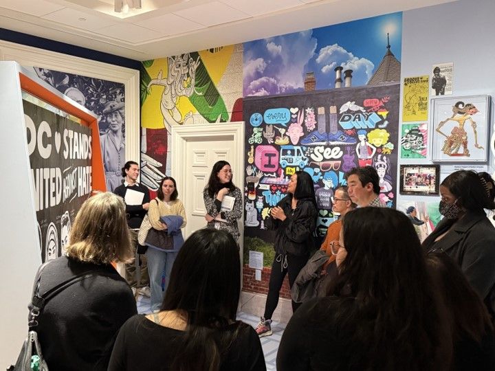 eople stand near a mural by the artist Cita Sadeli, and listen to her talking about why and how she made the mural.