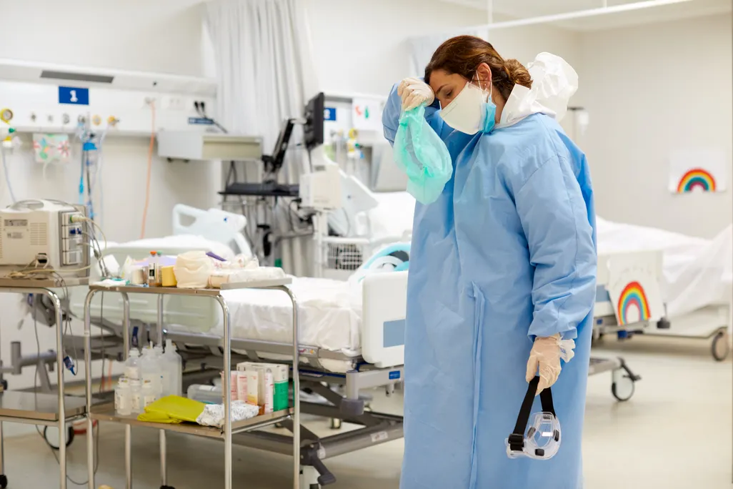 A female ICU doctor with a mask and gown wiping her forhead