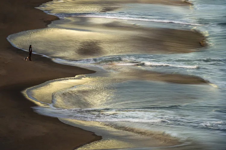 A woman walks with her dog at sunrise on the beach