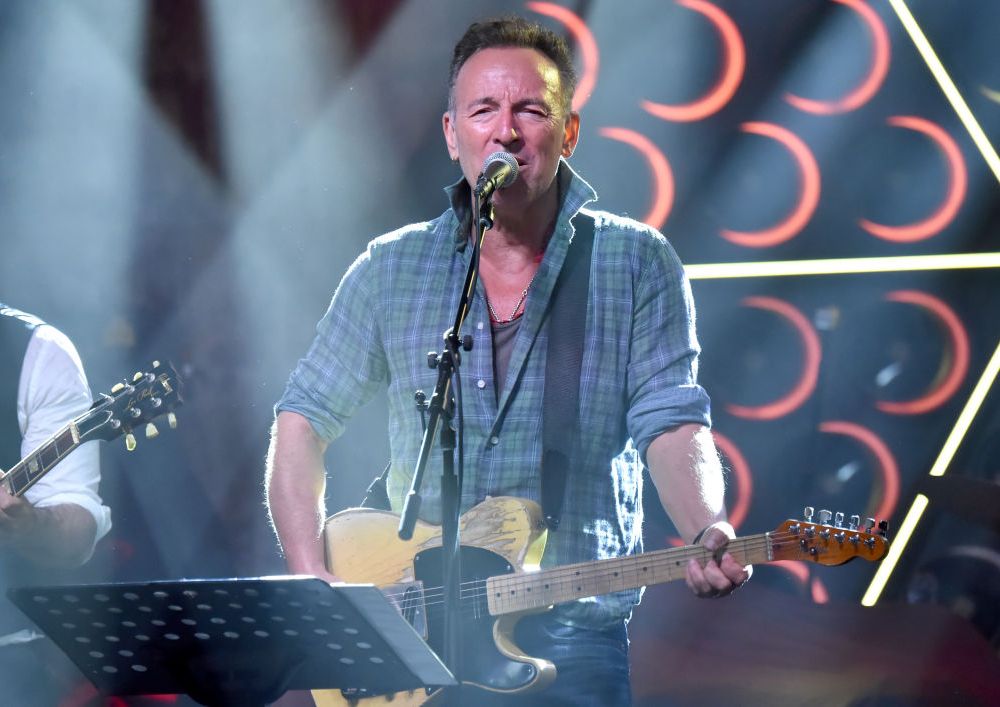 middle-aged man singing on stage into microphone and playing