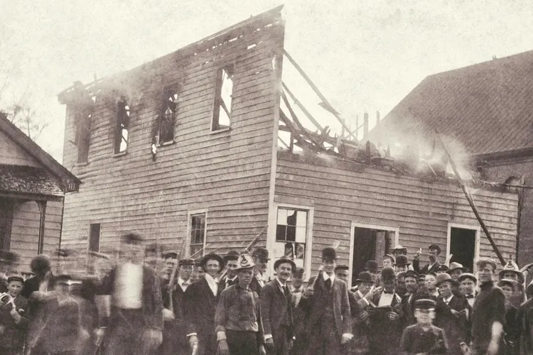 A white mob poses outside of the razed office of the Daily Record, a Black-owned newspaper in Wilmington, North Carolina.