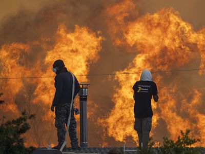 Flames reach the Greek village of Gennadi, where residents stand on roofs to try to save their homes with water hoses.