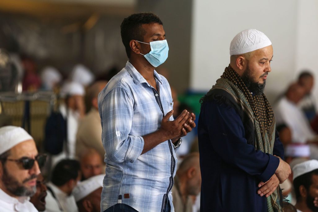 Muslim men pray at the Grand Mosque, one wearing a mask