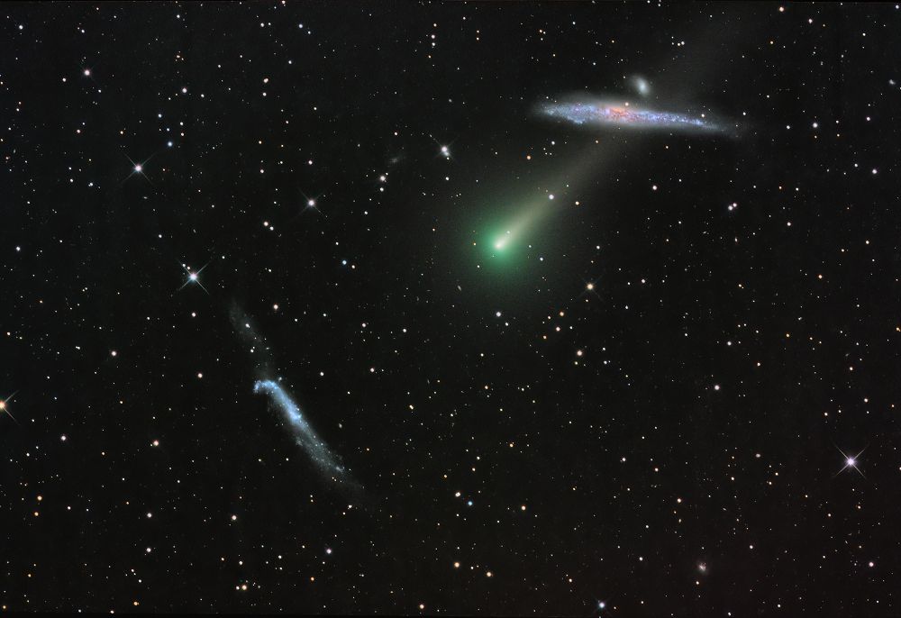 Photo of a comet whizzing through space. The comet is a bright blue orb with a tail behind it; stars fill up the background