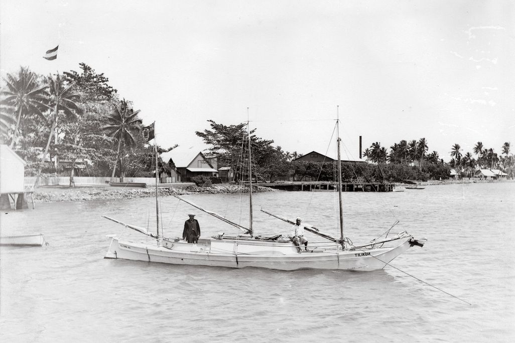 a black and white photo of two men standing in a  dugout sailboat