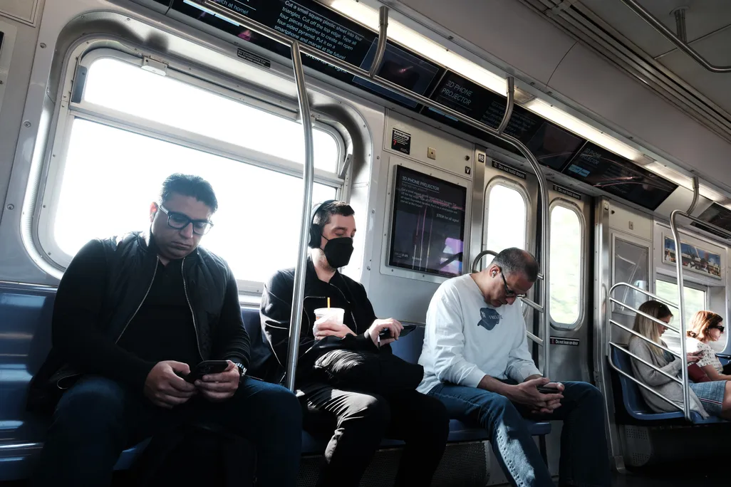 People sitting on a train, one with a mask on