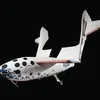 A white spacecraft against a black background. The fuselage is spangled with dark blue stars and black circles. A large wing is swiveled up away from the fuselage. The tail of the spacecraft is marked by this identifying number: N328KF.