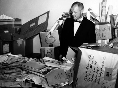 John Glenn stands in the NASA mailroom surrounded by thousands of letters sent to him.