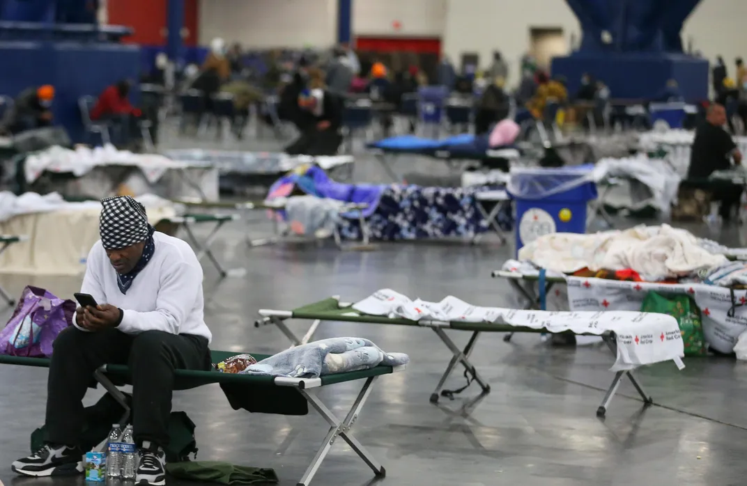 A man looks at his phone while sitting on cots in a convention center