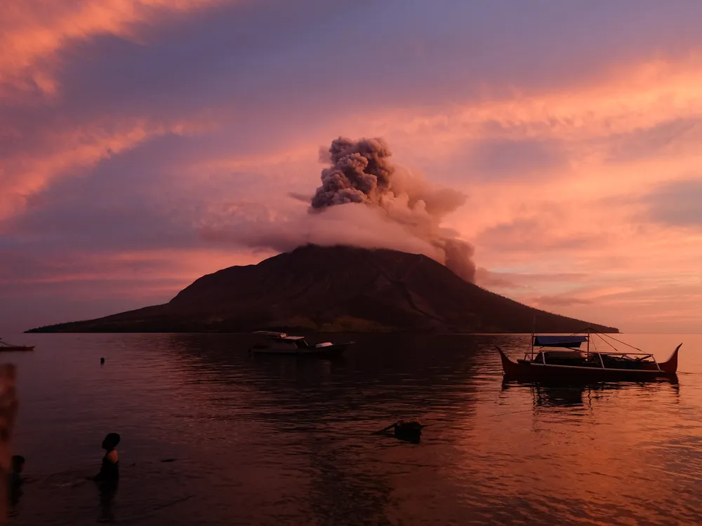 a volcano on an island spewing ash at sunrise