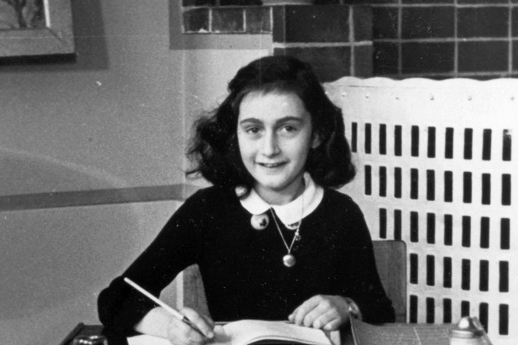 A young Frank sits at a school desk, notebook open and pencil poised to write, smiling and wearing a school uniform