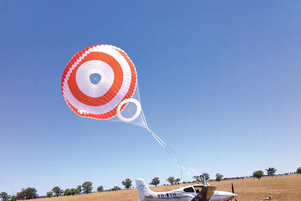 a parachute above a small aircraft only a bit above a field
