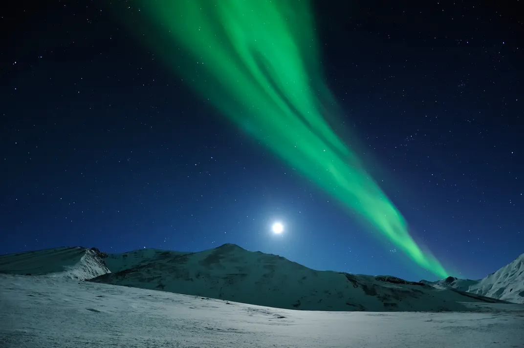 A brilliant aurora shines above a nearly full moon during a chilly winter night.