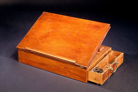 When the writing box is unfolded, it offers a slanted writing surface, a drawer to hold inkwells and quills, and plenty of room for paper.