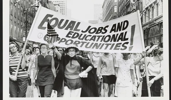 Women marching down the street holding a banner with the message “Equal jobs and educational opportunities!”