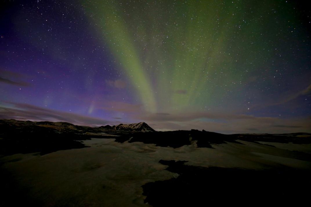 A photograph of the northern lights over a mountain in the distance.