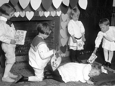 Admirers present valentines to a girl who is pretending to be sleeping, c. 1900s.  In the 18th and 19th centuries, British children celebrated Valentine's Day by going door to door, singing songs.