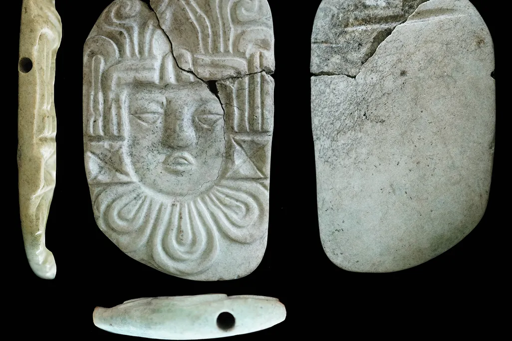 A side, front, back, and top view of a white carved pendant of a human head.