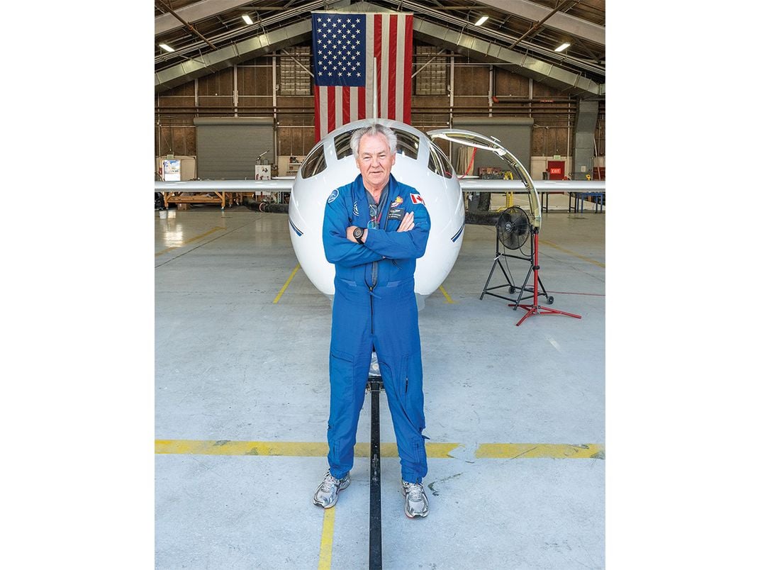 Bjarni Tryggvason standing, arms crossed, in a blue flight suit in front of plane