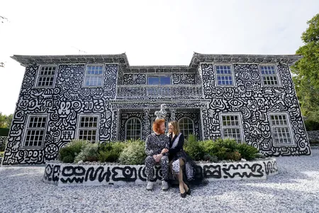 English artist Sam Cox and his wife, Alena, sitting in front of their Kent mansion, which Cox covered in doodles