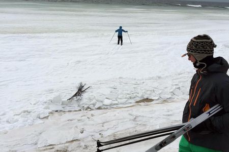 Skiing toward the breaking waves on a slush-covered beach.